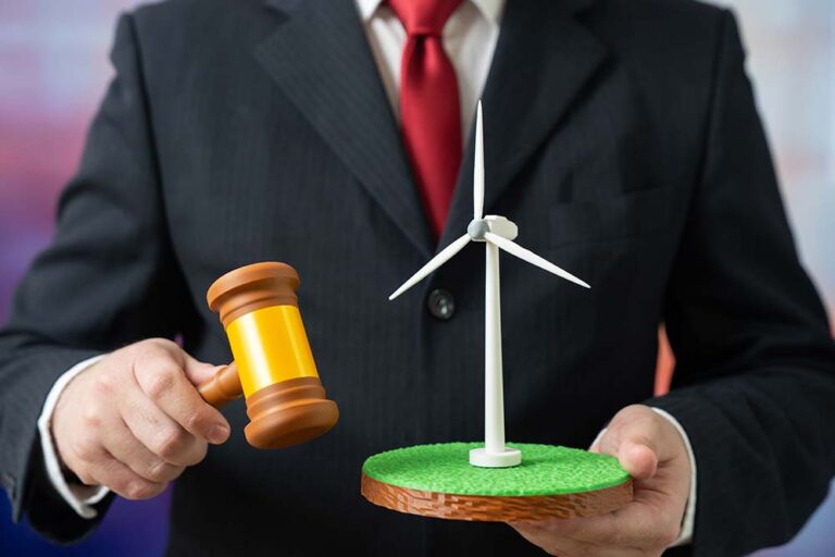 Environmental law - business man holding a gavel in one hand and a mock up of a wind turbine in the other