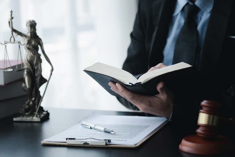 General law - a man sitting at a desk reading a law book, with lady justice in the background and a contract on the desktop